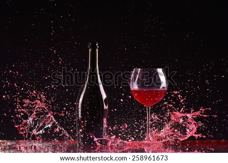 bottle and glass with red wine, red wine splash, wine pouring on table on dark black background, big splash around Glass and bottle of red wine splash on black