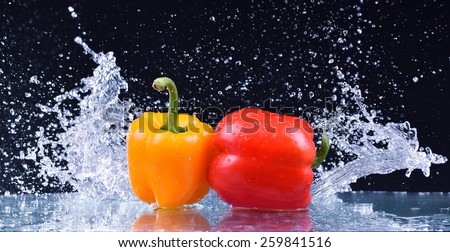 Macro drops of water fall on the red and yellow pepper and make splash
