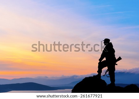 Silhouette of military soldier or officer with weapons at sunset. shot, holding gun, colorful sky, mountain, background
