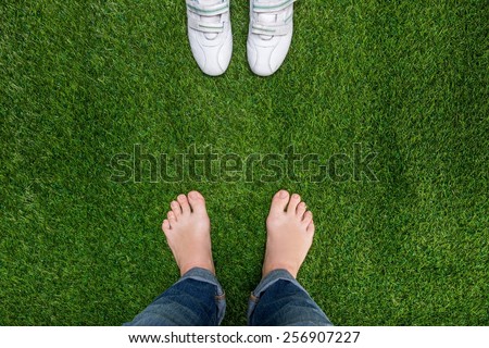 Feet resting on grass with sneakers standing opposit