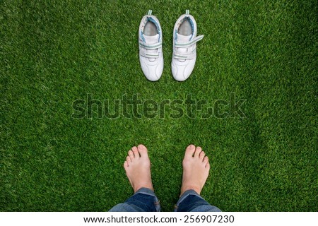 Feet resting on green grass with sneakers standing opposit