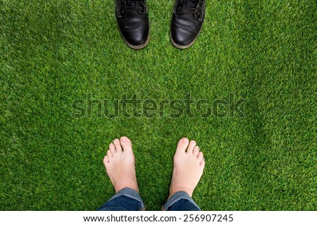 Mens feet resting on green grass with standing opposite boots