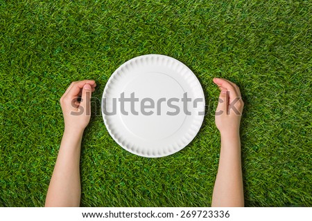 Human hands with empty plate on green grass
