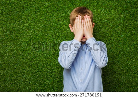Boy in shirt  hiding his eyes over green grass