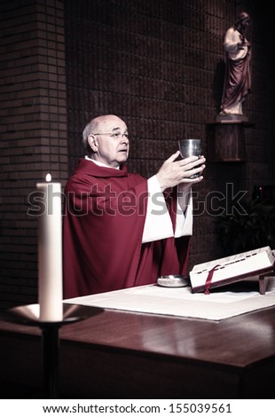 Priest in robe holds up a chalice of wine.