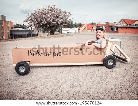 Young girl sitting in a soap-box car shaped like a piece of pumpkin pie.