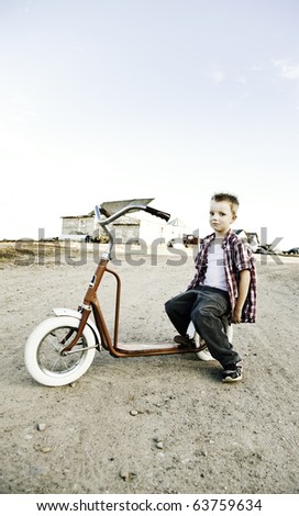 Image of a young boy sitting on a vintage scooter with a straight face.