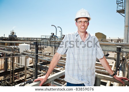 A portrait of a man wearing a hardhat and safety glasses in front of a industrial background