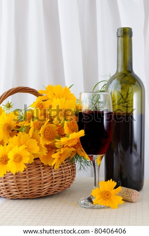 A glass of rose wine with an open bottle and yellow flowers in a basket