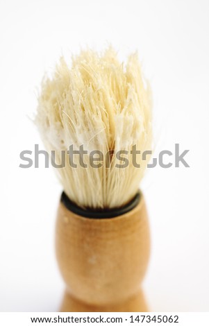 A shaving brush with shaving soap on the bristles on a white background
