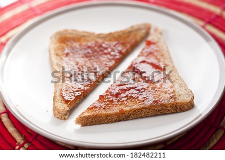 A slice of brown toast with strawberry jam cut diagonally