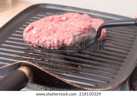 A spatula is used to flip over a burger patty cooking on a grill-pan