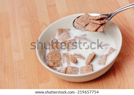 A spoon with malted cereal on it hovers above a bowl of cereal and milk