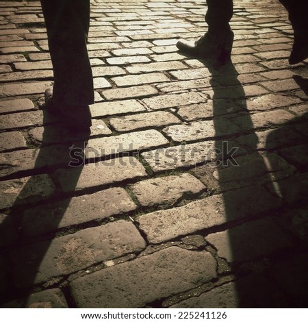 Image of persons walking over cobbled street in low bright sunlight, shot on a mobile phone with Instagram effect applied.