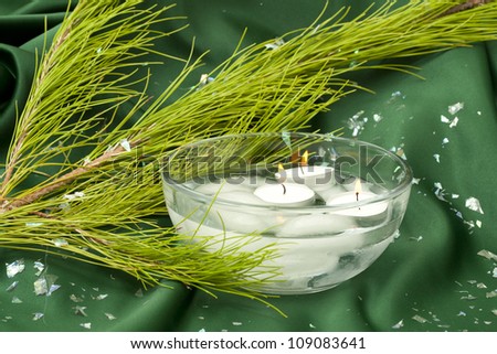 Bowl with candles and fir twig on green satin with confetti
