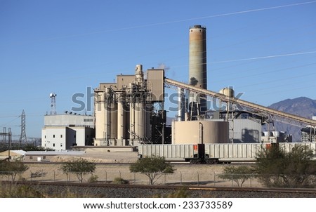 Industrial site with smoke pipe, elevator, delivery freight train cars and power lines running through blue sky