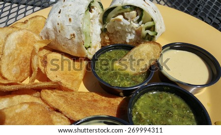 Flour tortilla wrap stuffed with rice and vegetables served with potato chips and salsa