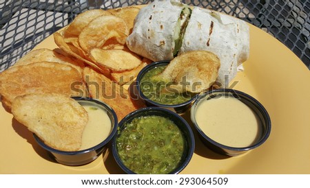 Lunch with wheat flour tortilla wrap, potato chips and green salsa