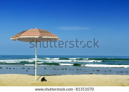 Beach sun shield umbrella and flip-flops at ocean water edge