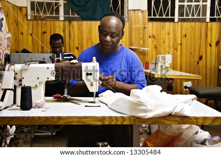 Two african man sewing in a small tailor shop, industrial sewing machine, African small industry