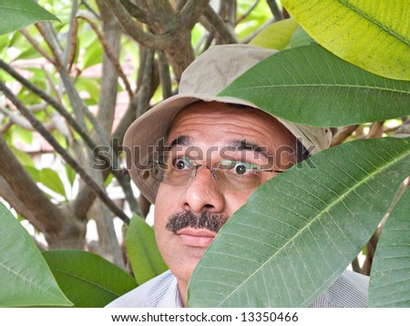 Private detective with sun hat hiding in the bushes