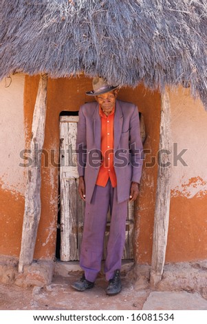 Portrait of elderly  african man with a broken had and old suit in front of the hut