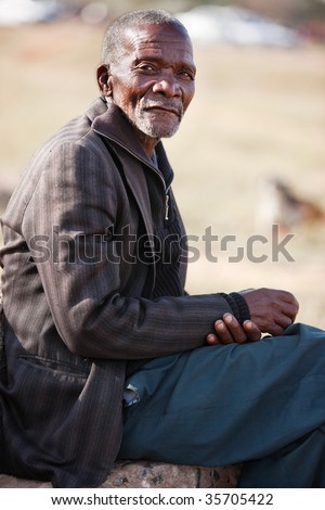 old African resting on a stone, blurred African desert background