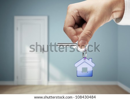 key with blue  key chain in hand against backdrop of rooms