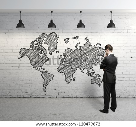 man looking at  world map on brick wall