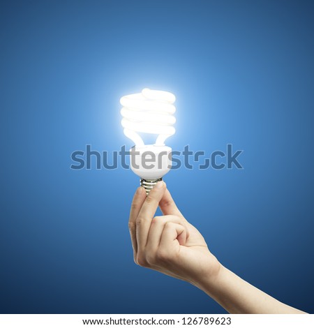 hand and energy saving lamp on blue background