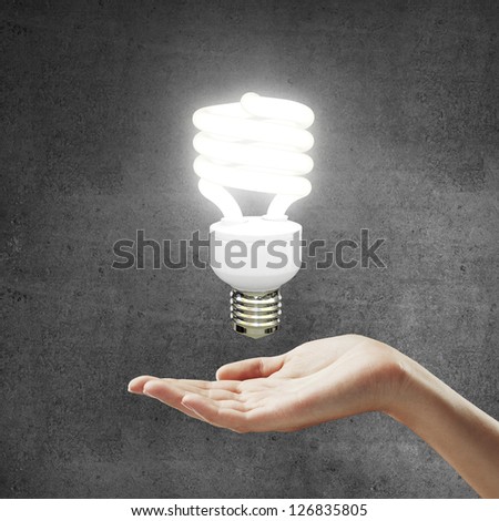 hand and energy saving lamp on gray background