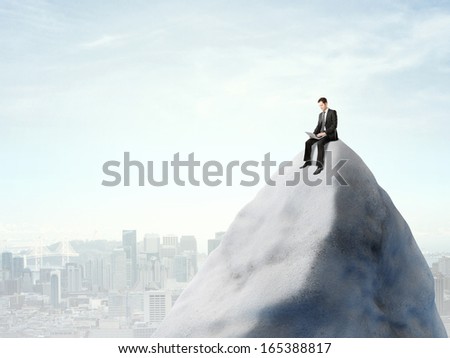 businessman sitting on top of mountain with laptop