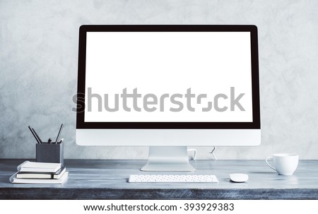 Empty white computer screen on wooden desktop with coffee cup and other items. Mock up