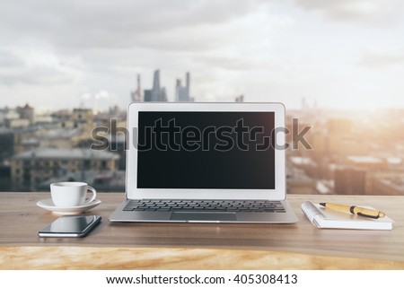 Wooden desktop with blank laptop, phone, coffee cup and notepad with pen on city background. Mock up