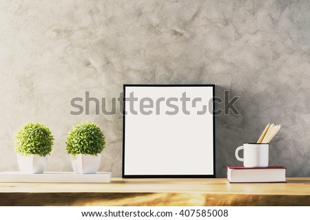 Closeup of wooden table with blank frame, two flowerpots, iron mug with pencils and book on concrete background. Mock up