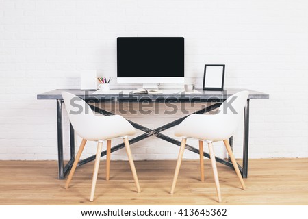 Two white chairs next to designer table with blank computer screen and other items on wooden floor and brick background. Mock up