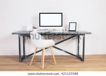Front view of modern chair and designer desk with blank white computer screen and picture frames on white brick background. Mock up