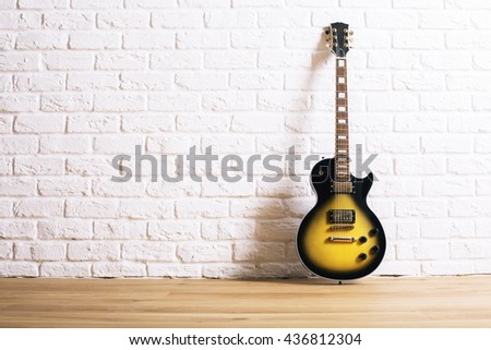 Black and yellow electric guitar in interior with wooden floor and white brick wall