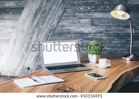 Wooden designer desktop with blank white laptop, stationery items, coffee cup, cell phone, plant and table lamp. Mock up