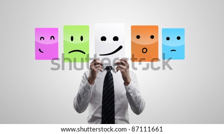 Business man holding a card with smiling face. Man chooses an emotional faces. On a gray background