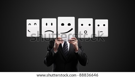 Business man holding a card with smiling face. Man chooses an emotional faces. On a black background