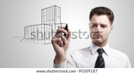 Young business man drawing a project of building on a glass window. Portrait of young architect thinking about construction. On a gray background.