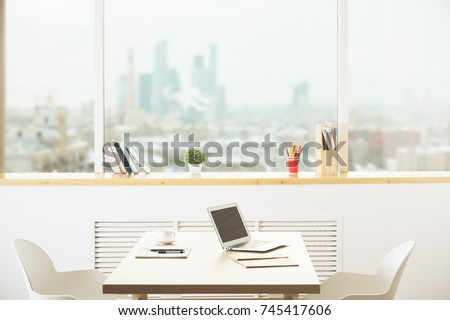 Side view of modern office workpace with laptop, supplies and other item in interior with blurry city view