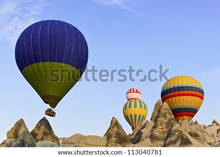 Hot air balloons captured coming over the limestone ridge in Caapadocia, Turkey. Weathered mineral peaks which have eroded through evolution present a backdrop to the striking colors of the balloons