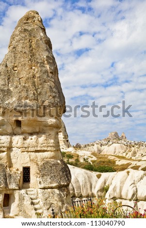 Vertical landscape of a ancient man made limestone residence from the Roman era. Backdrop is Uchisar on the hill, blue sky with cloudscape from the Goreme region of Cappadocia in Turkey