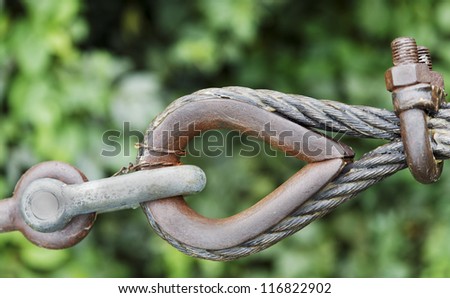 Generic eyelet and steel cables to guy ropes to strengthen a building structure, green leafy background, sunny day. Rusty metal which has been greased, angled concept shot
