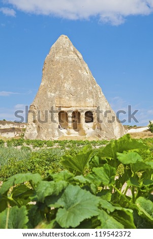 Vertical old limestone cave historically a community church and meeting place. Cushions for seating remain on patio. Surrounded by agricultural farmland with potato crops, shot  in Cappadocia, Turkey