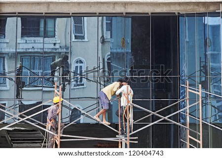 BOMBAY, INDIA - JULY 10, 2012: Builders on a scaffolding at work on a high rise building without safety harness or foot wear on July 10, 2012 in Bombay, India.