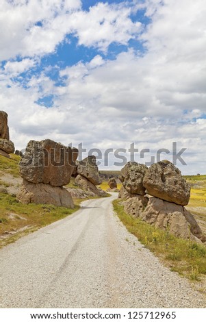 In the rural countryside of Turkey, volcanic activity left boulders perched precariously on either side of the dirt track graveled road. No signage that warns of avalanche. Shot location Cappadocia