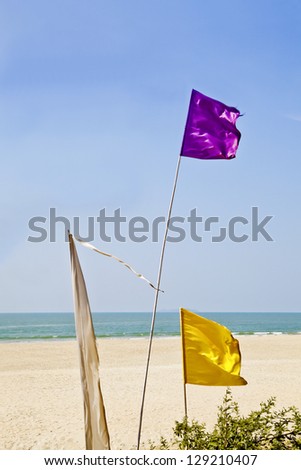 generic shot of colorful flags blowing in the breeze outside a shack restaurant in Goa India. Sandy beach with surf and coastline, picturesque idyllic scene